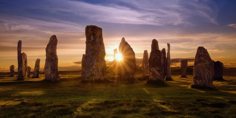 A group of stonehenge standing in a field at sunset