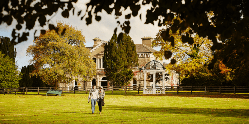 A couple of people on a walk in front of a mansion