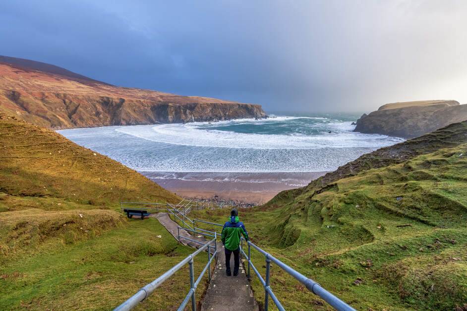 A person walking up a hill towards a body of wate
