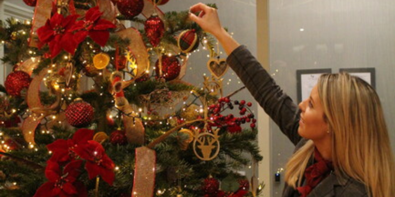 A woman decorating a christmas tree with red and gold ornaments