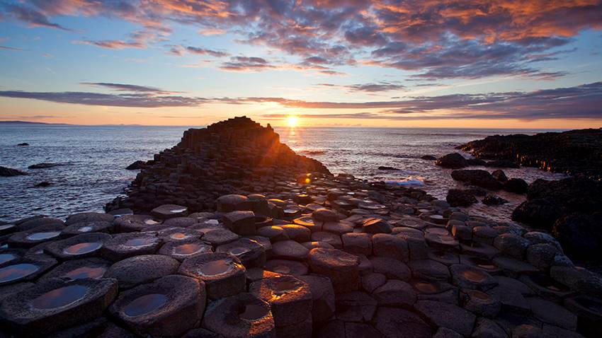 The sun is setting over a rocky beach