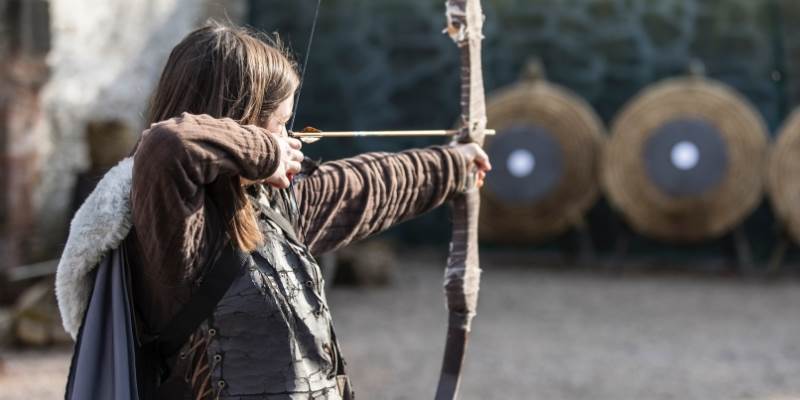 A woman dressed in medieval clothing aiming a bow