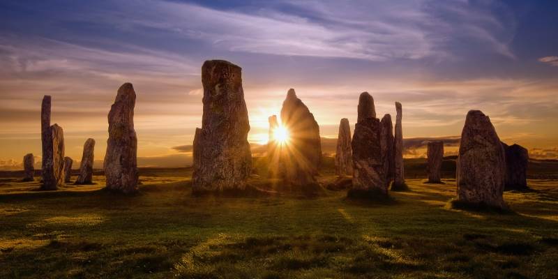 A group of stonehenge standing in a field at sunset