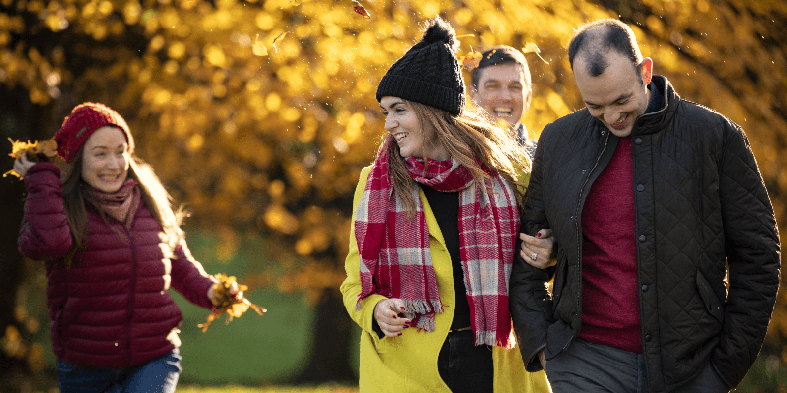 A group of people walking through a park in autumn