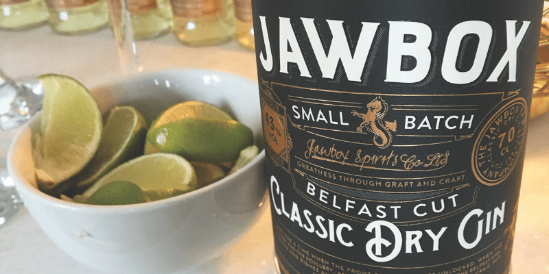 A close up of a bottle of gin near a bowl of limes