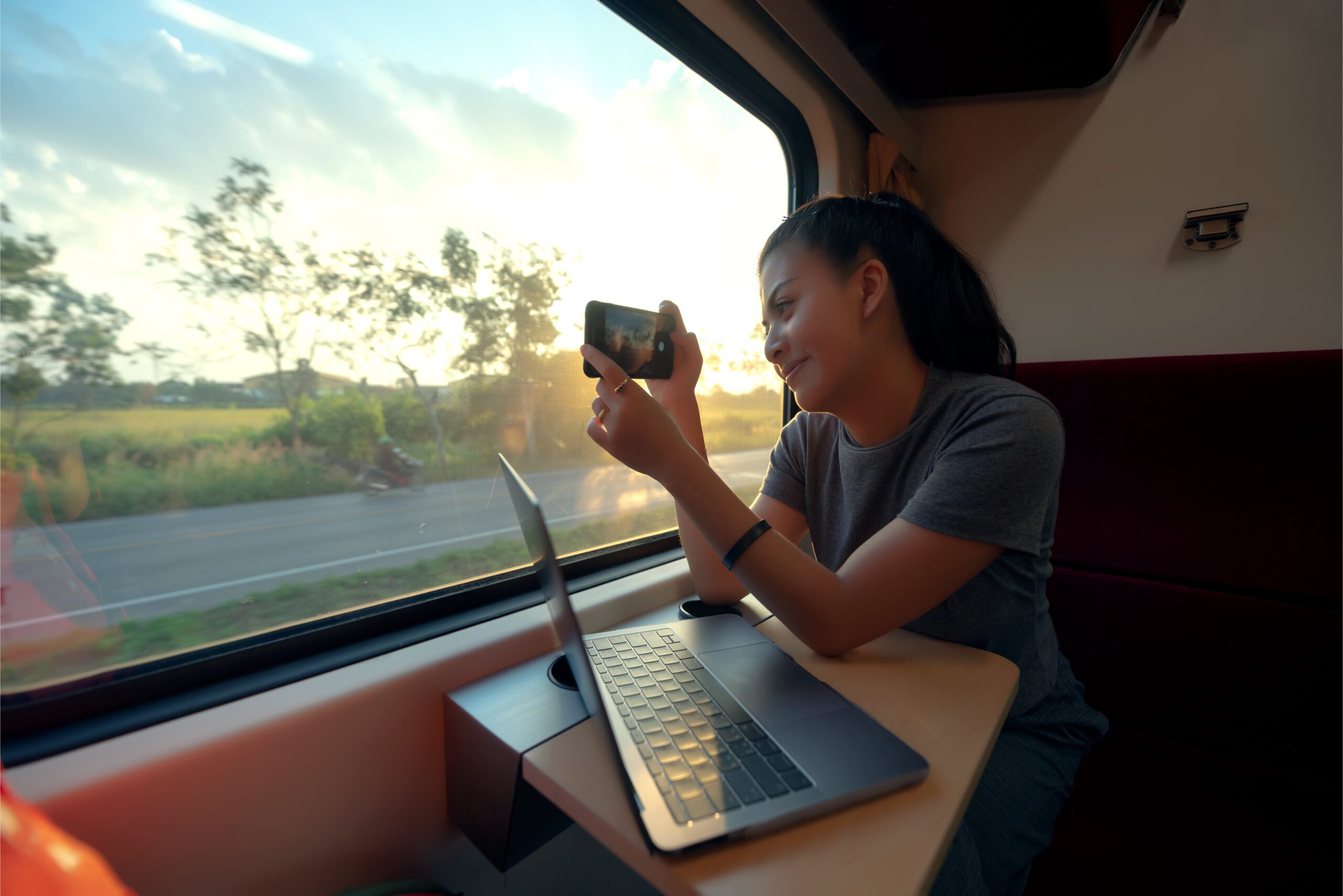 A woman on the train takes a photo on her phone while looking out the window of a train for a rail vacation trip.