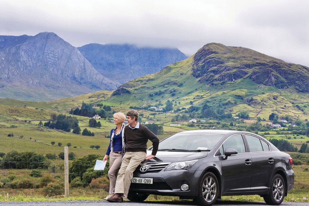 Woman and man sitting on the hood of a car in Ireland for a self-drive vacation.