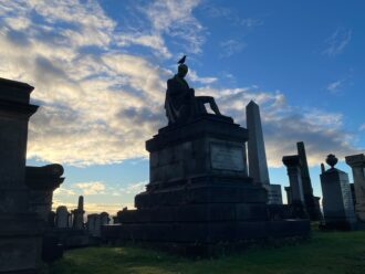 Historic tombstones in the Glasgow necropolis at early morning against a blue sky with some clouds