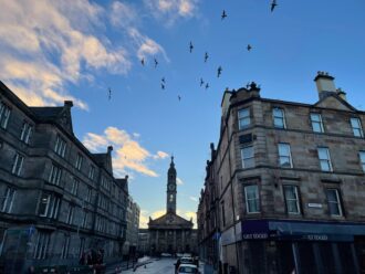 Birds take off in flight between historic buildings against and blue sky in Edinburgh in the early morning.