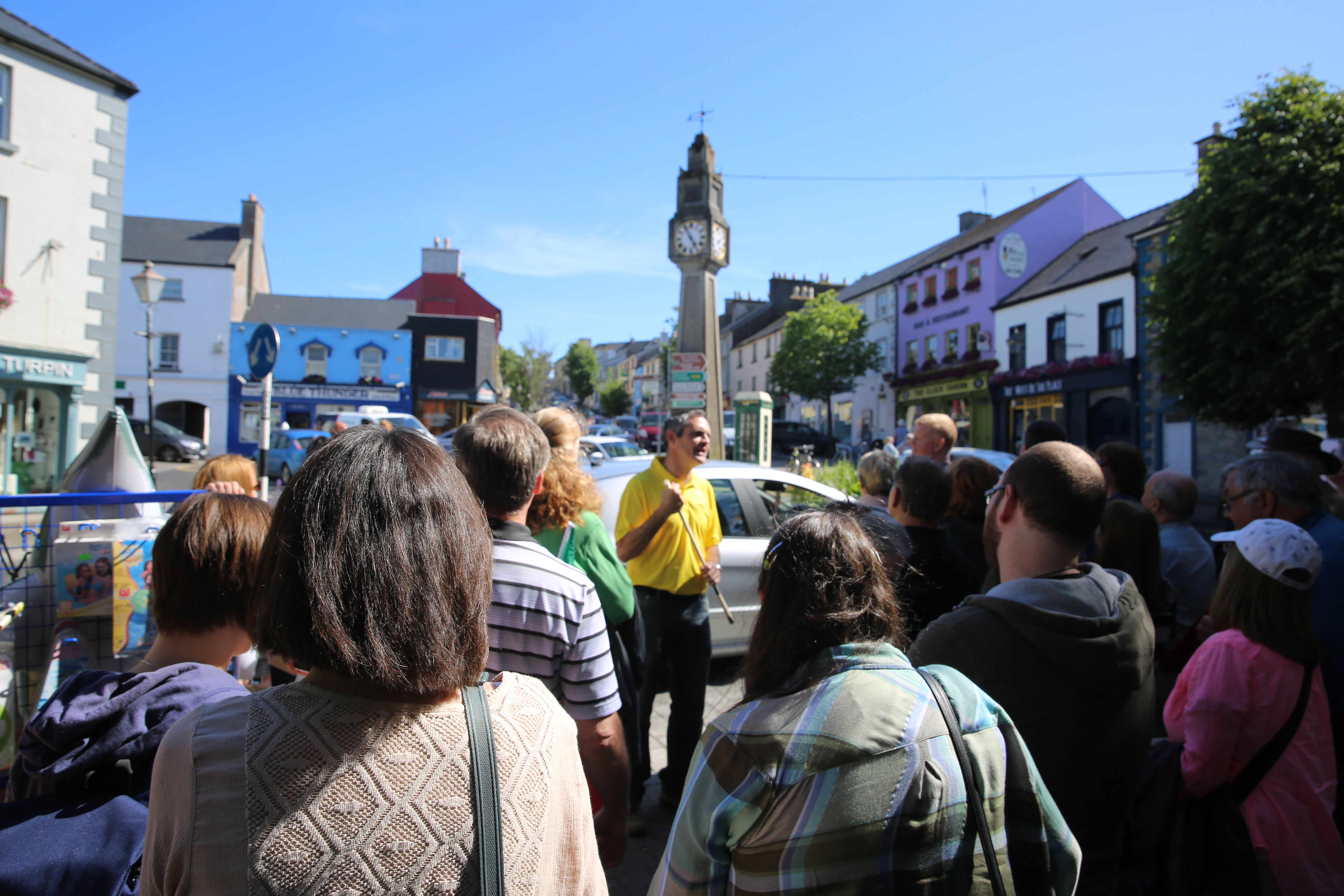 A crowd of people walking down a street next to a clock tower with a Local Specialist