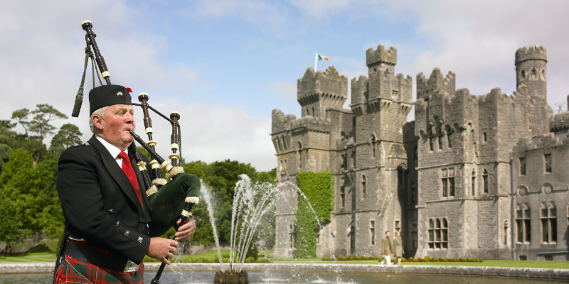 A man in a kilt playing bagpipes in front of a castle