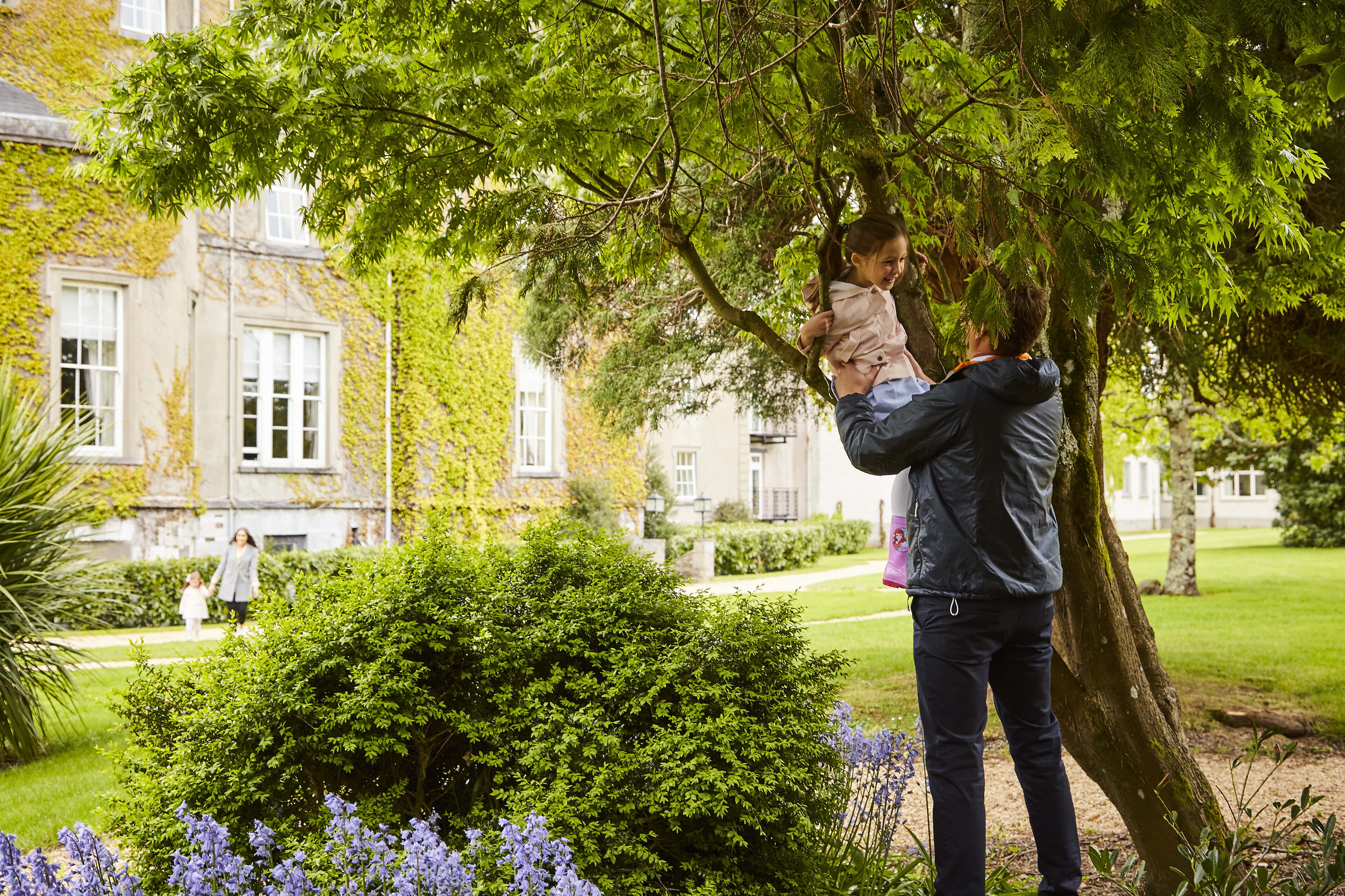 A man holding a child and playing in the garden of the Great Southern Hotel in Killarney