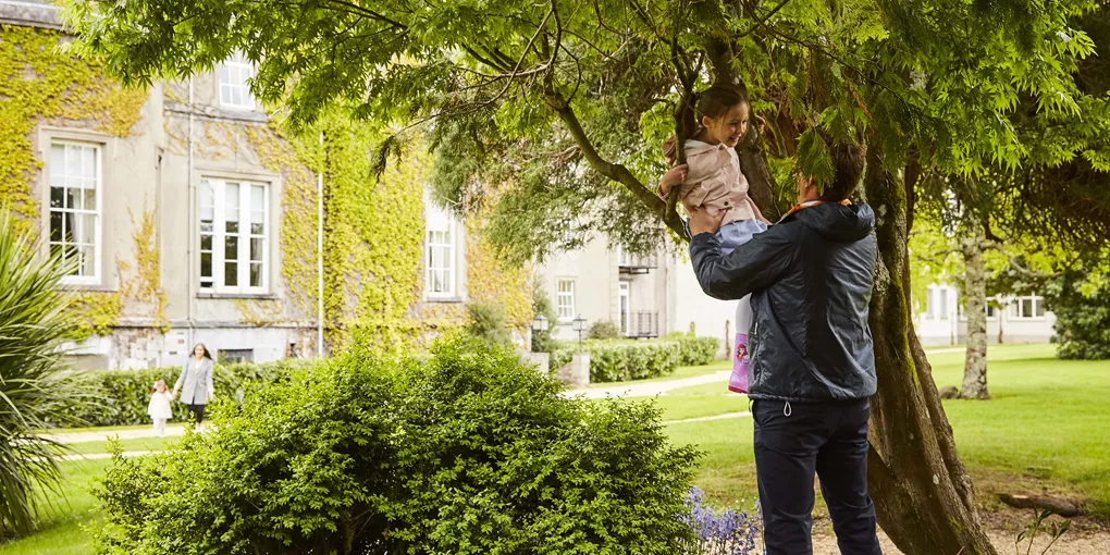 A man holding a child and playing in the garden of the Great Southern Hotel in Killarney