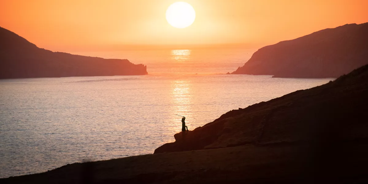Man with a sword on the mountain next to the river at sunset