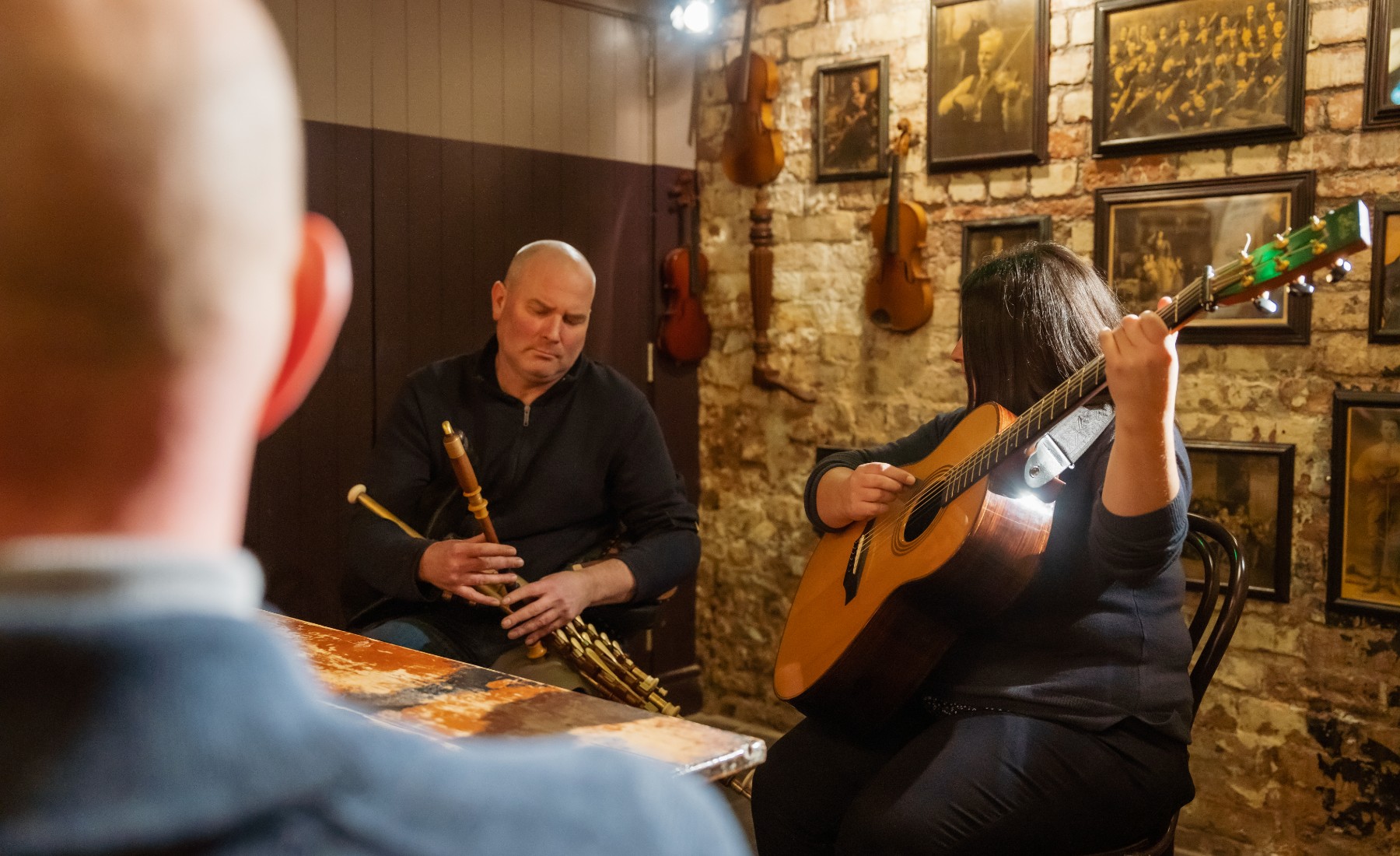 People playing acoustic instruments inside a cobbled brick house