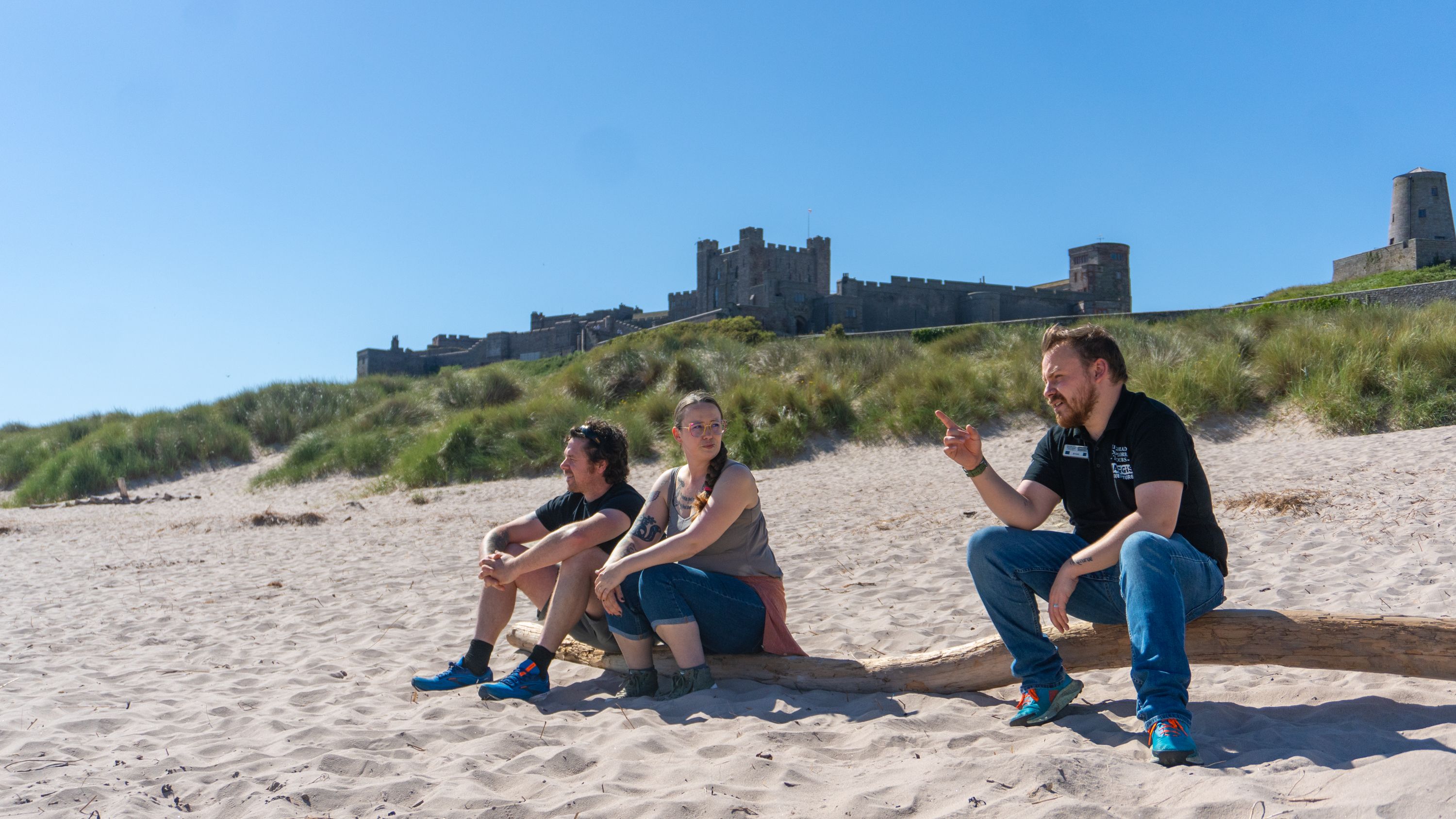 Two Men and A Woman Sitting On Sand Outside Alnwick Castle