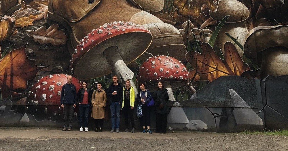 Group of people standing in front of a mural of mushrooms on a Brendan Vacations Glasgow street art tour