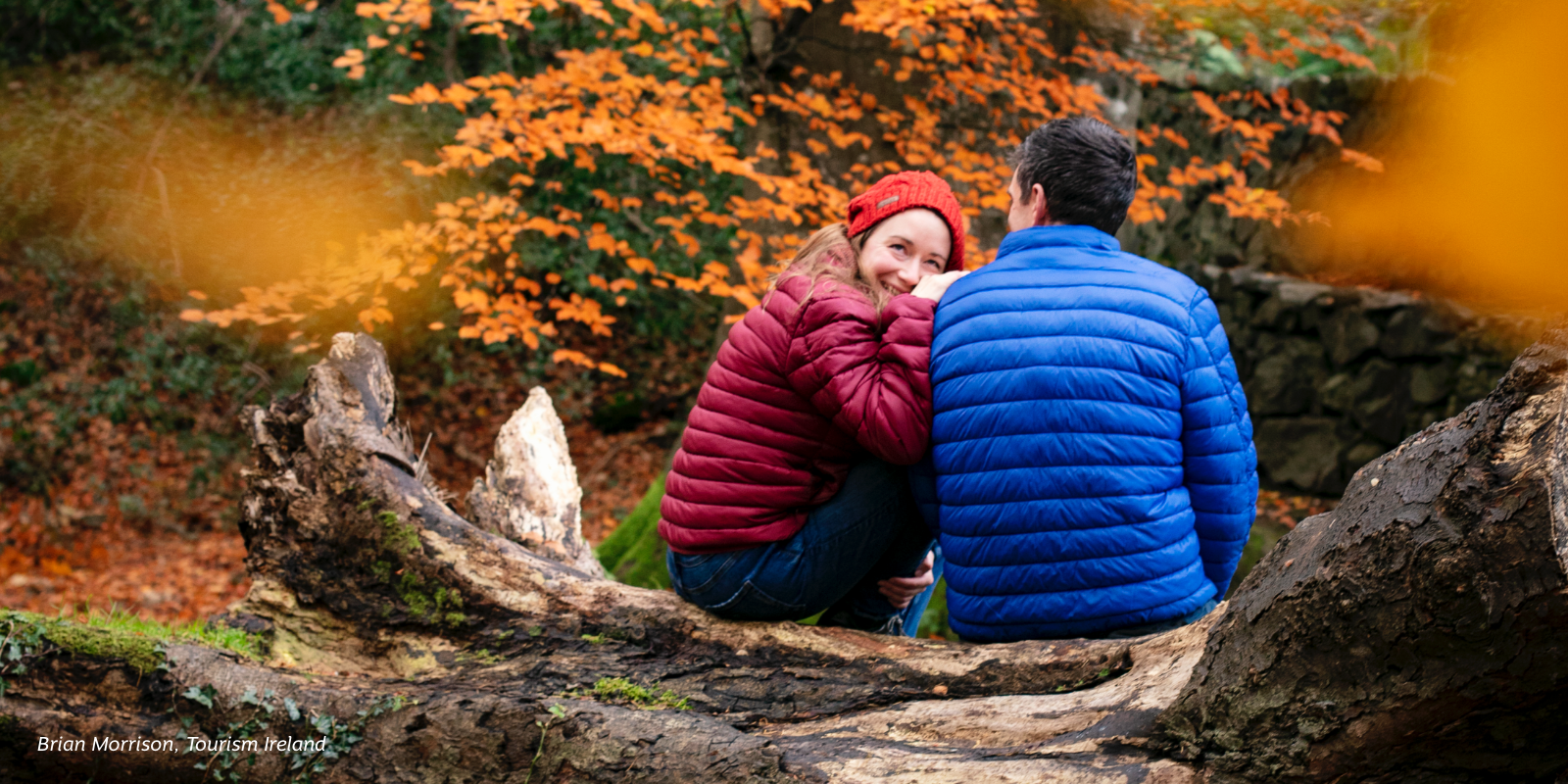 Couple sitting on log surrounded by autumn leaves