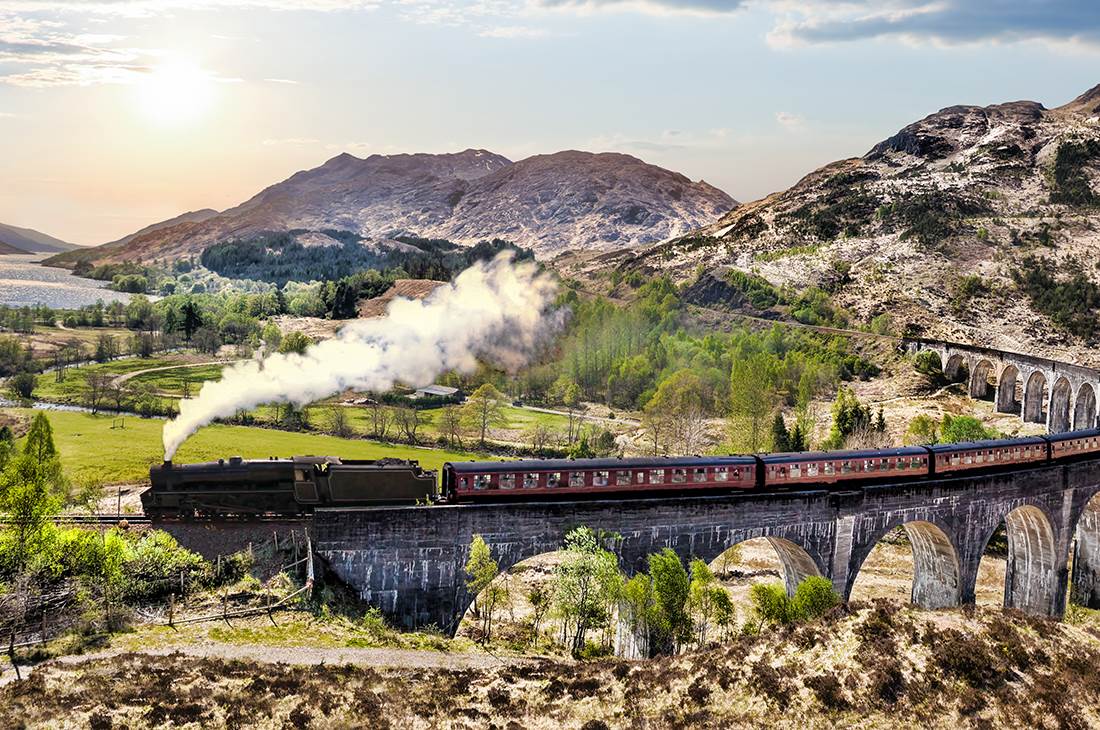 Steam train crossing a bridge among a rocky landscape