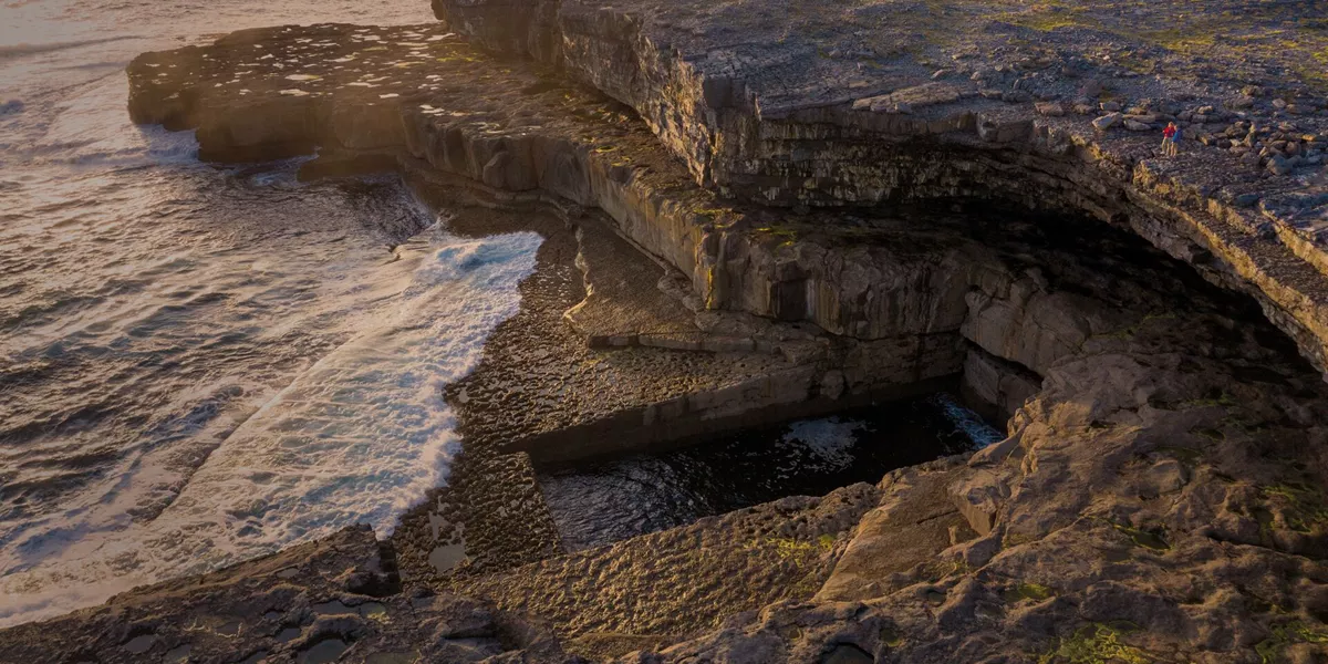 Sharp cliffs of the worm hole on aran islands, sea crashing against it.