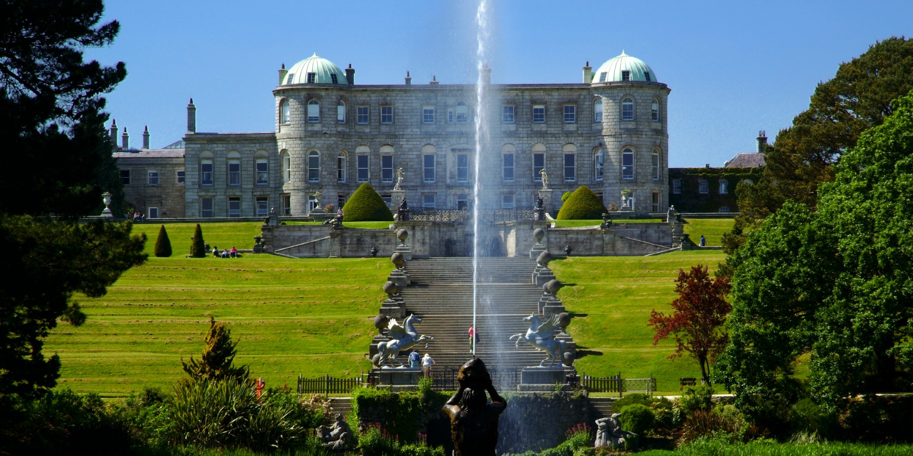 A fountain in a lake shooting water in the air with a large house in the background