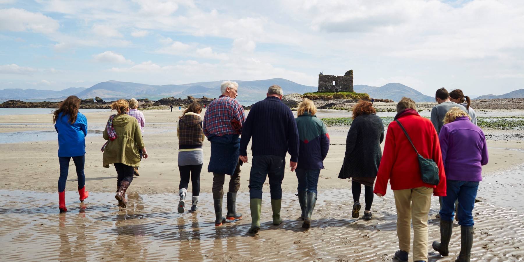 group of people walking towards ruins on the beach