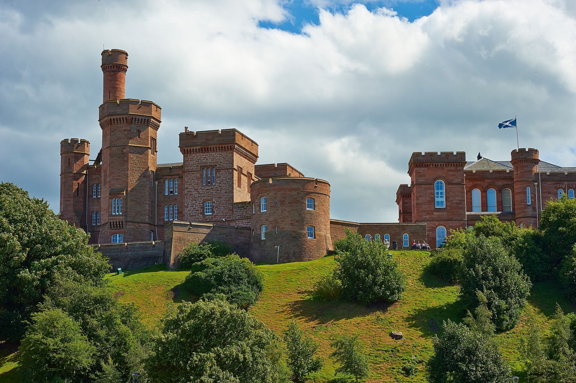 A red stone castle in Scotland's Highlands on a green grassy hill against a sky full of clouds.