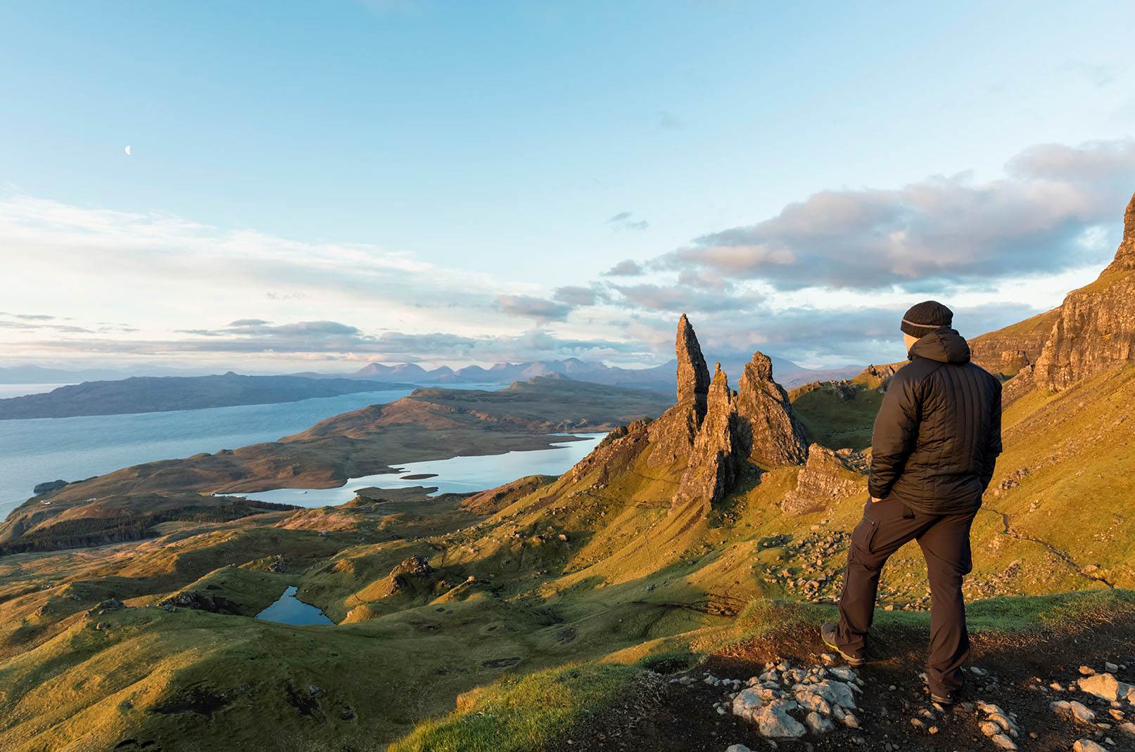 A man in a jacket and hat enjoys the view of the lake and rocks