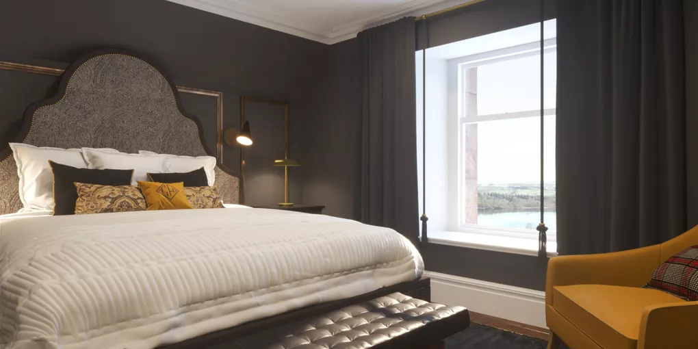 A bedroom with a large bed and a yellow chair in Cameron House, Scotland