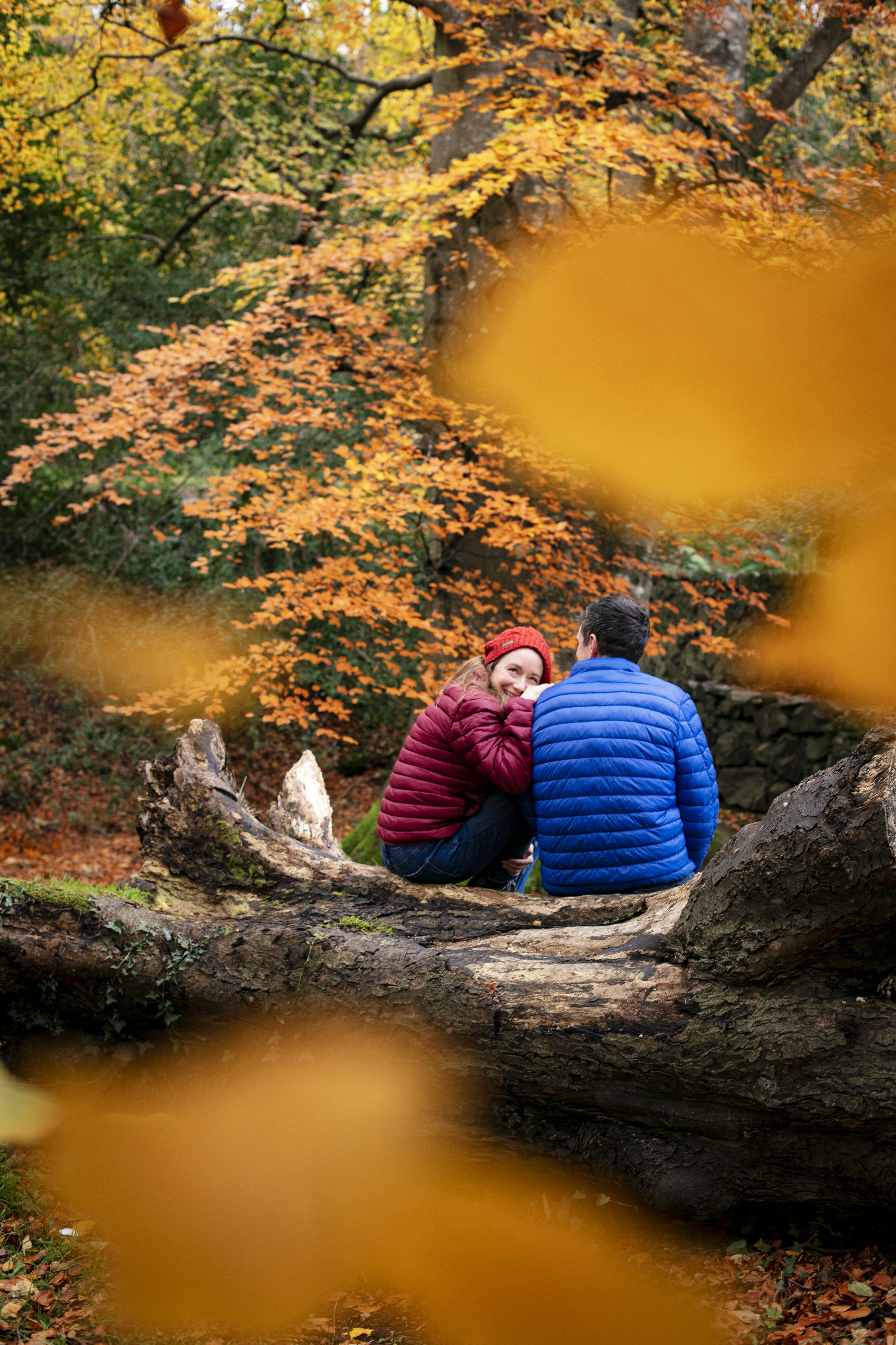 Couple wrapped up warm sitting within the autumn leaves