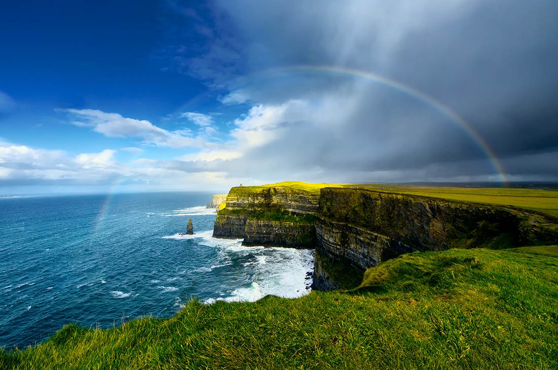 A rainbow over the ocean with a cliff in the foreground 