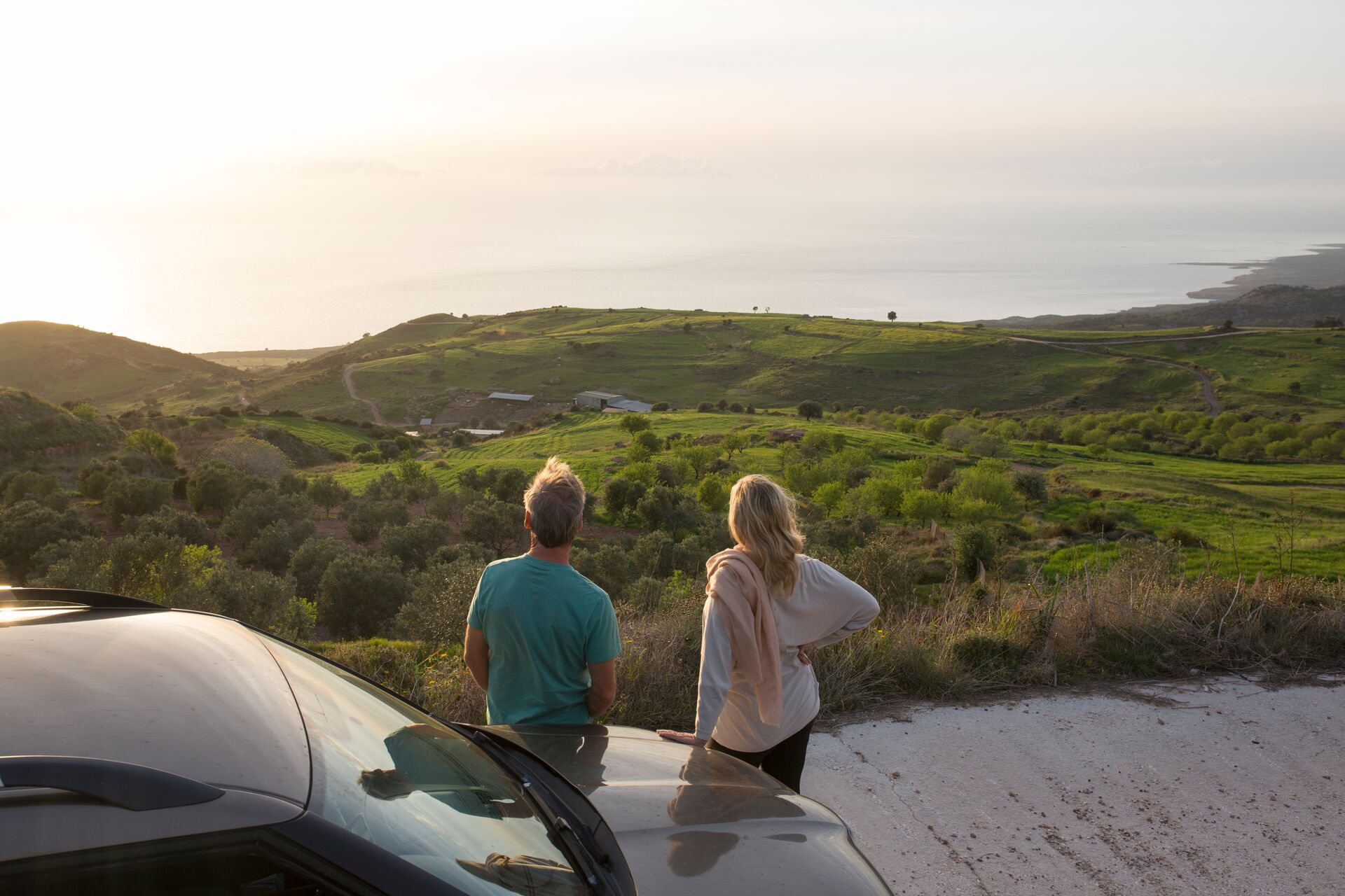 Couple pause at roadside to look upon sea and valley 