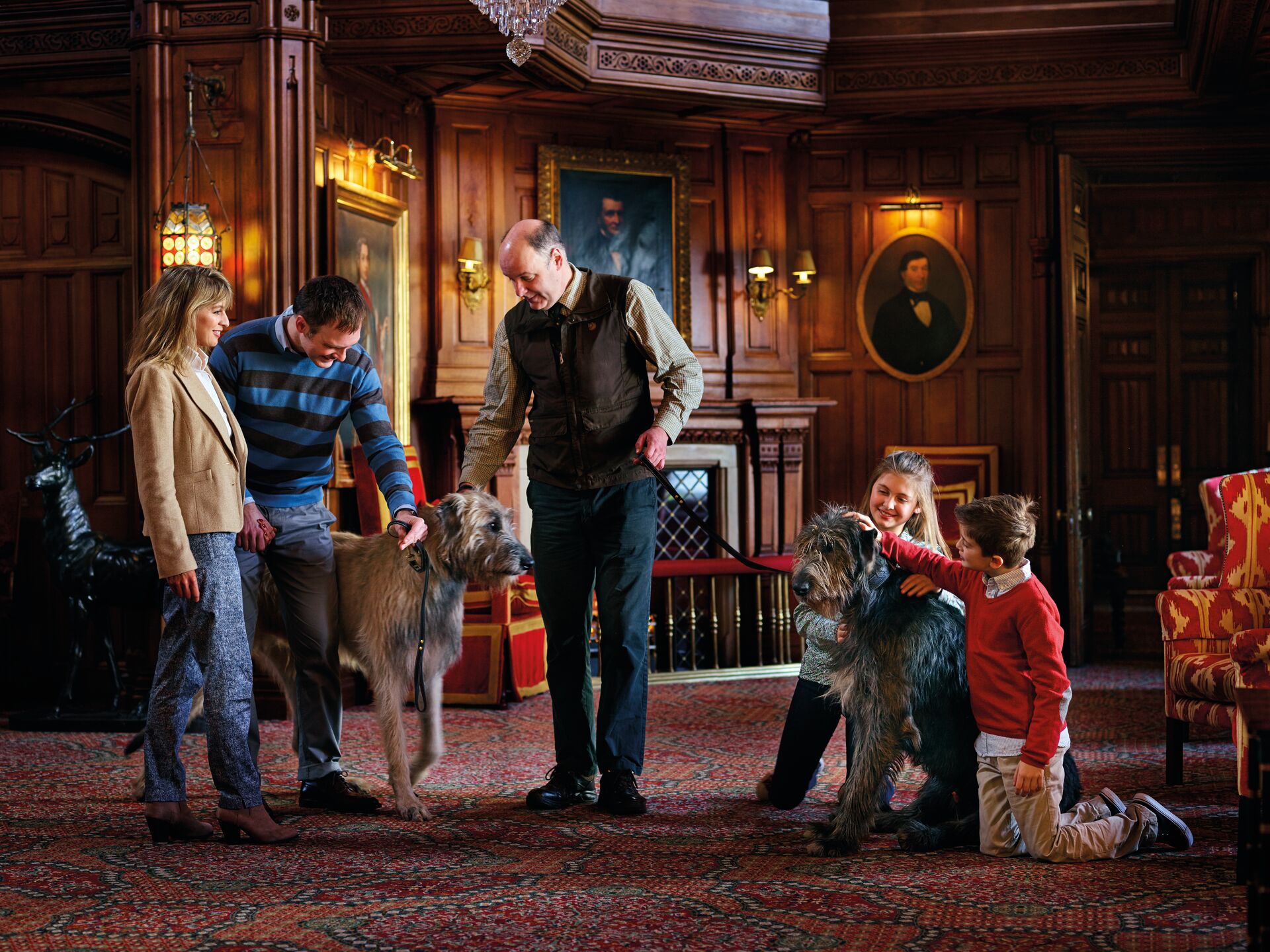 Family with two large wolf hounds in grand hallway of old house