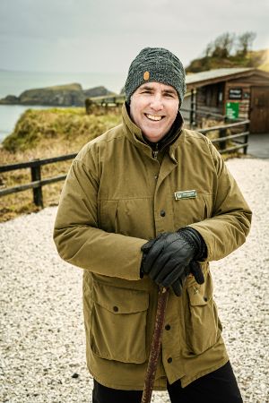 A man in a jacket and hat holding a stick