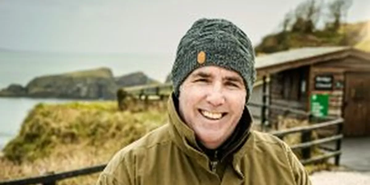 A man in a jacket and hat holding a stick