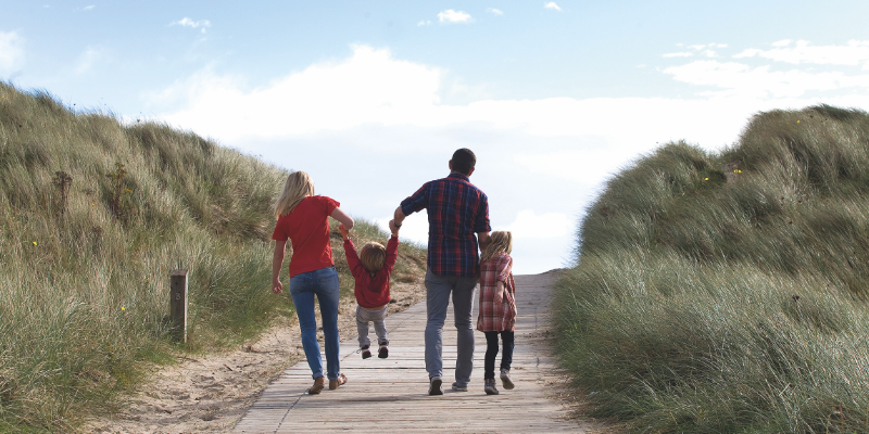 Family walking over a hill to the beach holding hands