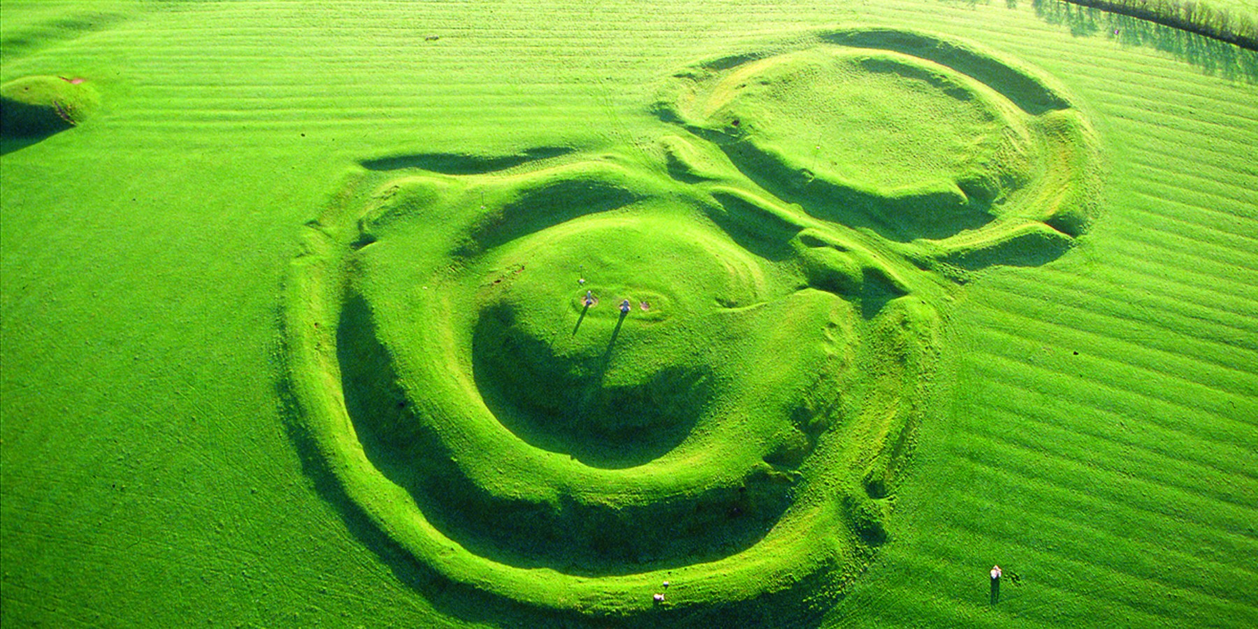 A bright green field, called the Hill of Tara, viewed from the air, with two interconnected circular ditches that are the sunken underground structures of the Hill of Tara which are in the heartland region of Ireland nearby Dublin