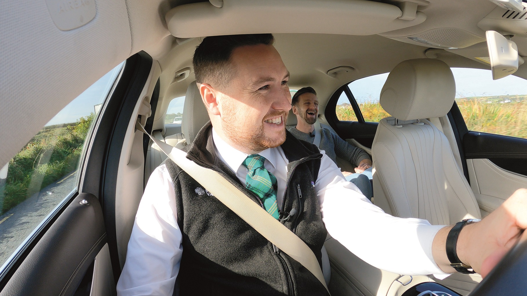 A man driving a car with another man in the back seat